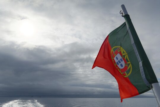 Portuguese flag waving majestically against a cloudy sky over the sea, Horta, Faial Island, Azores, Portugal