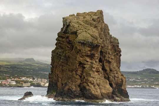 Imposing rock monolith 'Iieu em Pe' stands in the Atlantic Ocean off the coast of the island of Pico with the town of Madalena in the background, Iieu Deitado, Iieu em Pe, Horta, Faial, Azores, Portugal