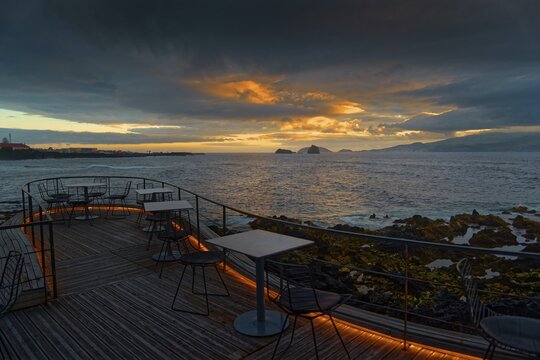Terrace of the Cella Bar overlooking the coast of Madalena and the distant island of Faial at sunset under dramatic clouds, Madalena, Pico, Azores, Portugal
