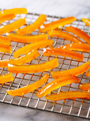 Candied orange peel strips cooling on rack. Marble background. Close up.