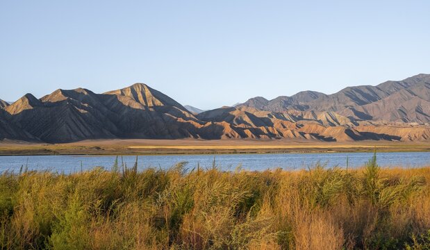 Blue Toktogul reservoir between dry mountain landscape, hilly mountains in the evening light, Jalalabad region, Kyrgyzstan