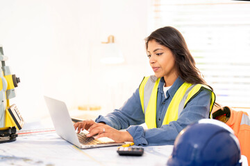Female land surveyor reviews plans while using smartphone and laptop during office hours at project site