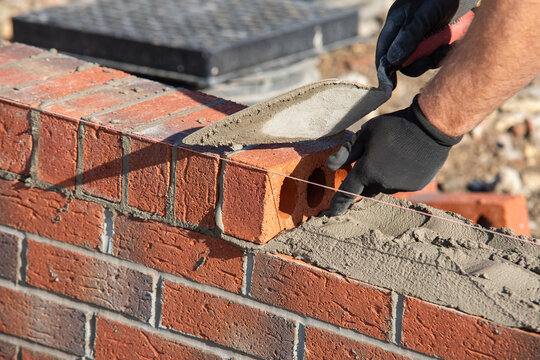 Close-up of skilled bricklayer working on construction site laying red bricks for wall construction  