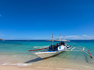 small local boats on turquoise tropical wave sea near philippines islands with beautiful sand beach on sunny day