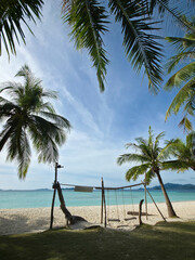 beautiful white sand beach with swing and palm trees on sunny day near turquoise tropical wave sea. philippines islands. vertical