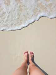 young woman legs and feet staying on beautiful white sand beach on sunny day near turquoise tropical wave sea. philippines islands. vertical