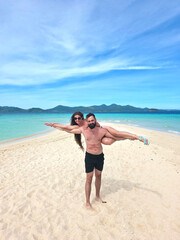 young beautiful woman with long hair lies on the shoulders of her handsome man with a beard and they smile on the coast of turquoise sea in philippines islands. vertical
