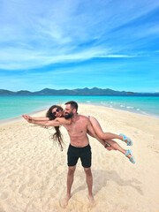 young beautiful woman with long hair lies on the shoulders of her handsome man with a beard and they smile on the coast of turquoise sea in philippines islands. vertical