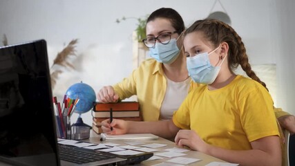 Teacher helping student wearing mask study at desk with laptop and book stack while tutor points to worksheet and student writes learning notes during online school session with globe pencil and - Powered by Adobe