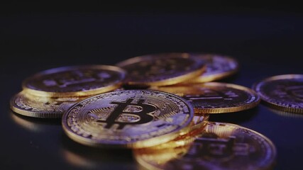 Shiny stacks of round metal coins bearing a bold B-shaped emblem rest in a dark, reflective surface