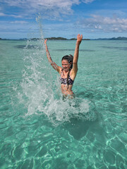 happy young woman in turquoise wave sea in philippines islands on sunny day. asia vocation. vertical