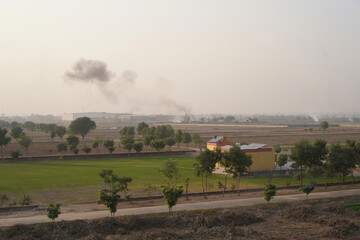 Black smoke from an industrial chimney. Straw and dry grass burning on land plots near the factory. Air pollution, smog in the suburbs, beige sky on a sunny day. Environmental pollution. Copy space.