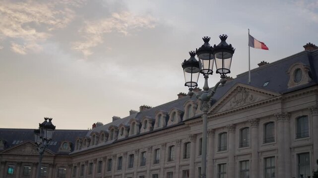 Exterior shot of a building in Paris France with the French flag waving in the wind The architecture is classical with ornate details and street lamps in the foreground Shot at dusk.