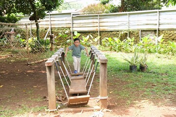 Child exploring a nature playground with a wooden bridge, highlighting scale, independence, and environmental awareness.