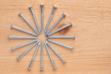 Group of shiny new steel construction nails neatly arranged in a circle on a natural wood background. Close-up. High resolution