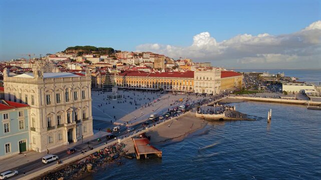 Drone footage shows Praca do Comercio from above with riverside promenade, moving crowds and iconic Lisbon buildings, highlighting scale, symmetry and urban space