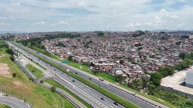 Vis&atilde;o a&eacute;rea de favela &agrave; beira da rodovia evidencia o contraste entre infraestrutura vi&aacute;ria e ocupa&ccedil;&atilde;o urbana informal.