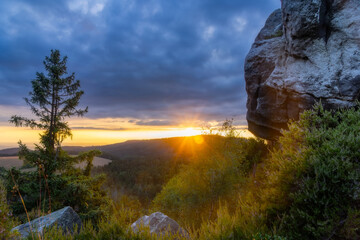 Sunset on the top of Naroznik (Table Mountains, Klodzka Valley, Lower Silesia Voivodeship). Dark clouds and sun flares forming a circle on the green bushes.
