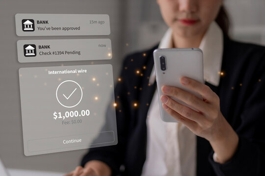 Asian adult woman manages international wire transfer via smartphone mobile banking application professional financial transaction approval notifications office setting