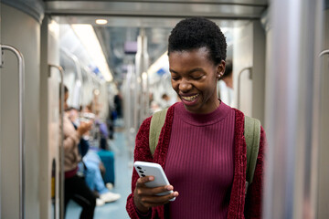 Young black woman smiling using phone on subway