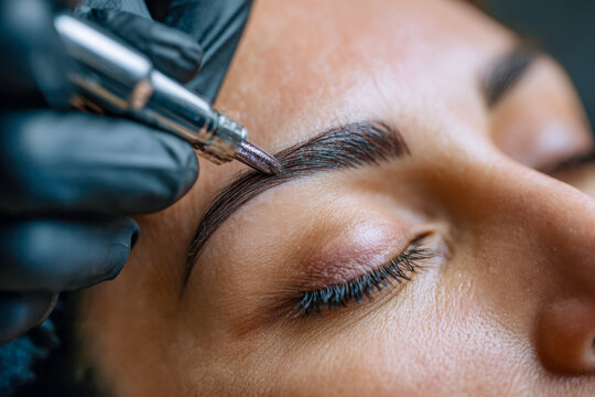 Professional eyebrow tattooing procedure enhances natural brow shape and fullness with detailed precision on a relaxed client?s face