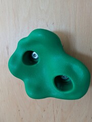 Green plastic climbing wall hold isolated on wooden surface, indoor sport and fitness equipment.