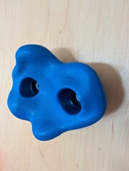 Blue plastic climbing wall hold isolated on wooden surface, indoor sport and fitness equipment.