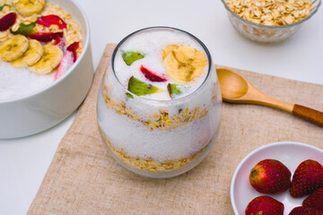 Refreshing yogurt parfait layered with crunchy oats, topped with sliced banana, kiwi, and strawberry pieces in a clear glass.