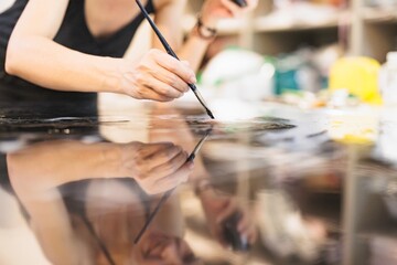 A focused artist delicately applies paint with a brush, creating stunning details on a surface. The studio is alive with colors and tools, showcasing the creative process