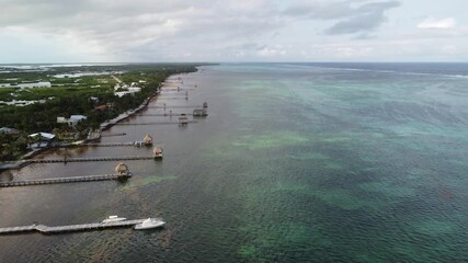 Aerial Drone View of Caye Caulker Island with Mangroves and Turquoise Sea, Belize.  Aerial drone shot of Caye Caulker Island in Belize, showcasing lush green mangroves, coastal houses, sandy paths.

