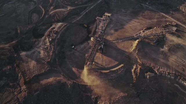 Wide aerial view of a massive bucket-wheel excavator operating in an open-pit coal mine. The giant mining machine continuously digs, extracts coal and soil, and transports material via long conveyor.