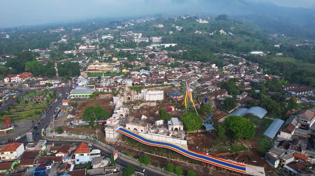 Aerial drone footage on top of Bandungan city in Semarang region, Java island, Indonesia, with Ungaran mountain in the background, an attraction park, and the town square