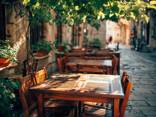 Wooden tables and chairs lined up on a sunny cobblestone street under lush green foliage creating a warm and inviting outdoor dining atmosphere