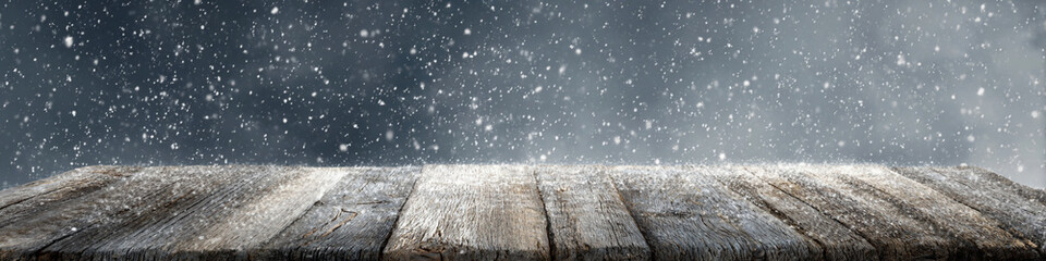 Gray weathered wood table surface with light snow and heavy snowfall in the background