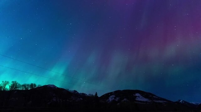 Shimmering northern lights over mountains power lines 