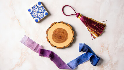 Artistic Still Life Composition Featuring a Blue and White Ceramic Tile, Wood Slice, Decorative Tassel, and Ombre Ribbon on a Textured Marble Surface for Creative Projects