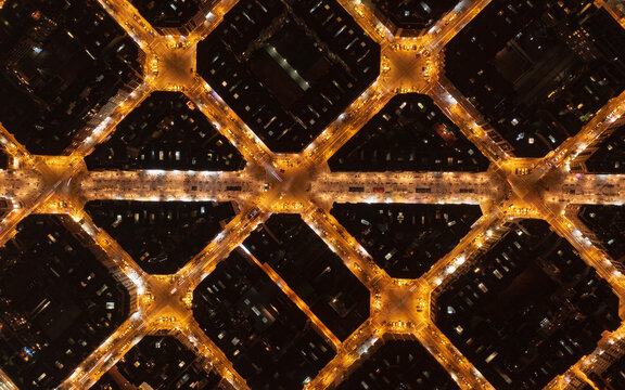 Aerial view of a grid of golden city streets, glowing with warm light against the dark night, Barcelona, Spain.