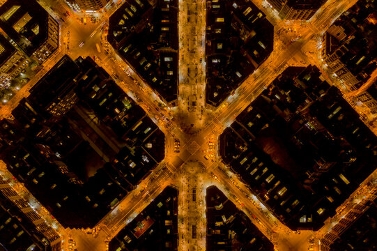Aerial view of a grid of golden city streets, glowing with warm light against the dark night, Barcelona, Spain.
