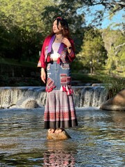 Beautiful Asian woman in modern Hmong traditional dress standing by a waterfall.