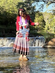Beautiful Asian woman in modern Hmong traditional dress standing by a waterfall.
