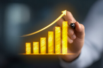 Businessman drawing a glowing golden bar chart with an upward trending arrow symbolizing growth, success, and positive financial progress in a blurred background set