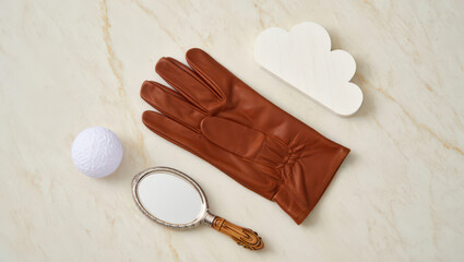 Artistic Still Life Composition Featuring a Leather Glove, Cloud Cutout, Golf Ball, and Hand Mirror on a Marble Textured Surface for Creative Visuals