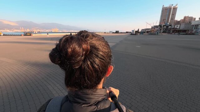 A walk along the paved embankment of Novorossiysk. Rear view. Bodycam footage. Back of a man's head with long hair. Golden hour. Wide angle. Atmospheric B-roll