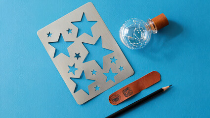 Artistic Still Life Composition Featuring a Star Stencil, Glass Bottle with Constellation Design, Leather Strap, and Pencil on a Vibrant Blue Surface for Creative Projects