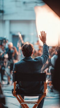 Behind-the-scenes moment of a film director guiding a scene, seated in a classic wooden chair with raised hand, capturing the creative process of movie production