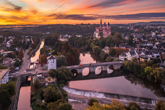 Aerial view of the serene Lahn river reflecting the vibrant sunset sky, with the majestic Limburger Dom standing tall, Limburg an der Lahn, Hessen, Germany.