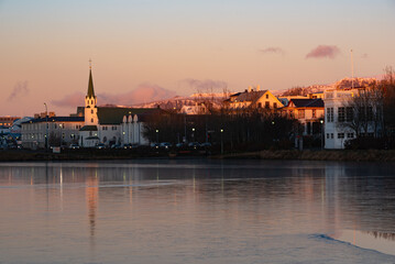 Obraz premium Reykjavík skyline at sunset reflected on Tjörnin pond with Hallgrímskirkja rising above the city in a peaceful evening scene