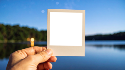 Hand holding an instant photograph of a beautiful starry night sky with the Milky Way galaxy over a calm lake and forest. Blurred background creates a beautiful contrast and focus effect.
