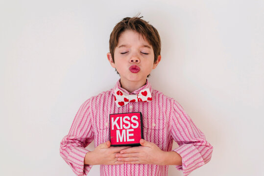 Portrait of a Smiling boy with his eyes closed puckering his lips while holding a Kiss me box