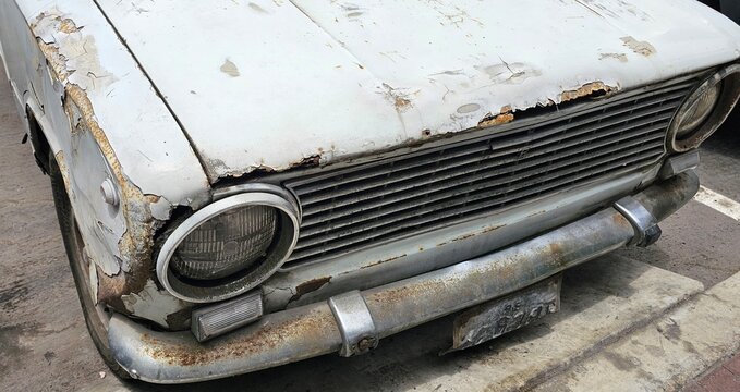 Front view of an old rusted car parked on the street